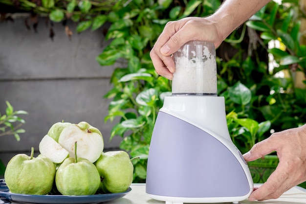 Hand van mensen gebruikt een elektrische blender om vers guavesap te maken.