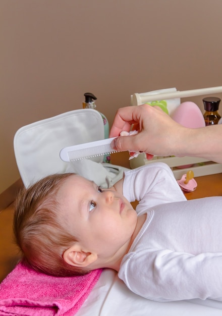 Hand van moeder die haar baby kamt die met een kinderkam ligt