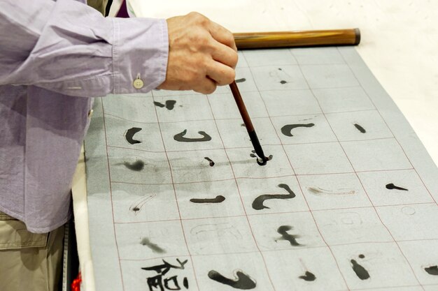 Foto hand van persoon die chinese borstel en demonstratie chinese brieven op stof houdt.