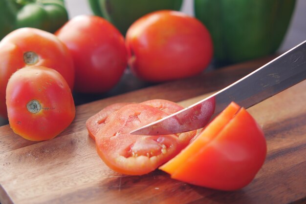 Hand van persoon die tomaten op snijplank snijdt