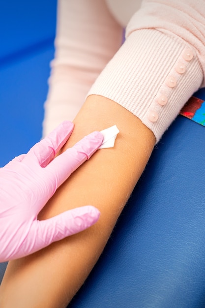 Hand van verpleegster wattenstaafje toe te passen op de arm van een jonge vrouw na een bloedmonster
