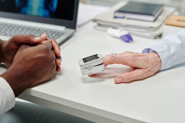 Hand van volwassen vrouwelijke patiënt met pulsoximeter op vingertop op bureau