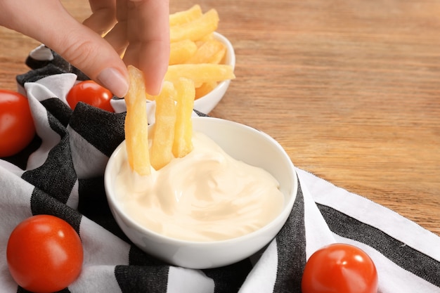 Hand van vrouw die frietjes eet met smakelijke mayonaisesaus, close-up