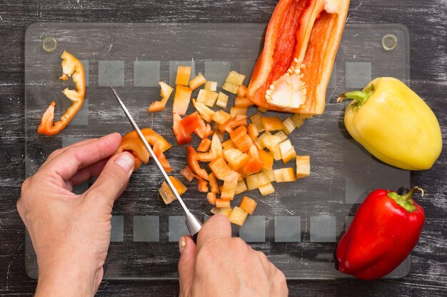 Hand van vrouw die verse peper met mes snijdt op het snijbord van glas op de zwarte achtergrond