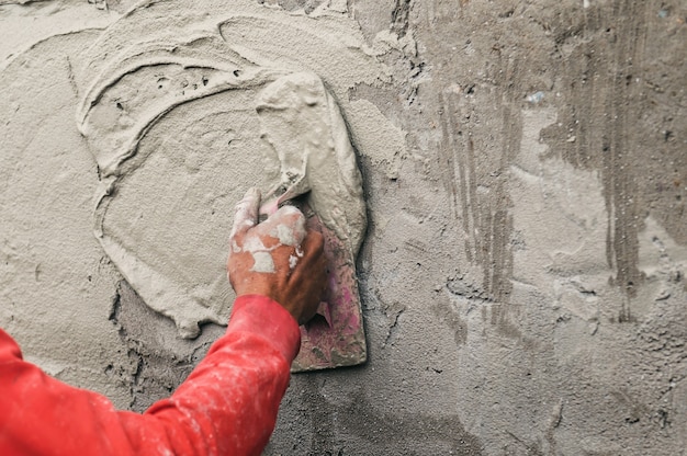 Hand van werknemer die cement aan de muur pleistert voor het bouwen van een huis op de bouwplaats