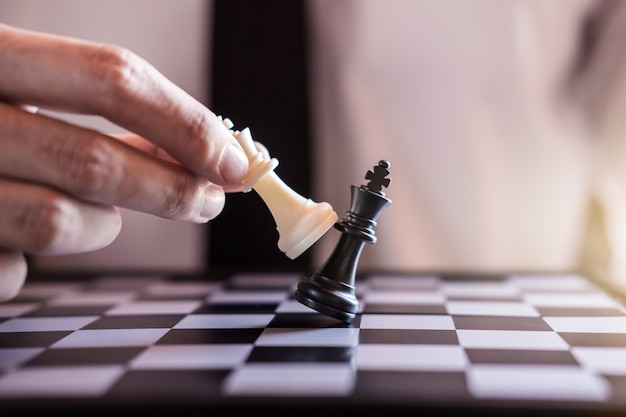 Hand van zakenman gebruik koning schaakstuk wit speelspel te omverwerpen de tegenpartij
