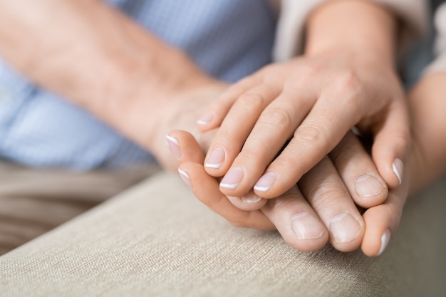 Hand van zieke gepensioneerde man tussen die van zijn zorgvuldige jonge dochter die liefde en genegenheid uitte