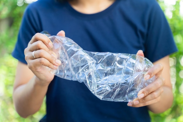 Hand vasthouden en verpletterende plastic fles voor recycle. In tuin achtergrond.