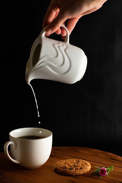 Hand vrouw melk gieten aan koffiekopje op houten tafel met zwarte achtergrond