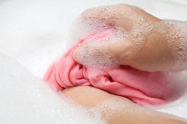 Hand washing clothes with bubble on white basin.