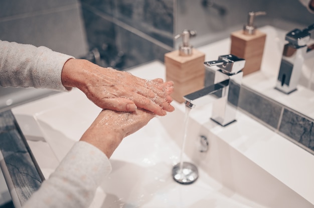 Photo hand washing lather liquid soap rubbing wrists handwash step senior woman rinsing in water at bathroom faucet sink.