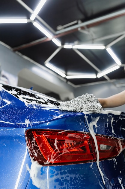 Photo hand washing with microfiber glove with foam car body in garage car washer doing manual foam washing in auto detailing service