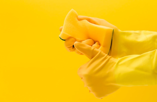 Hand wearing a yellow rubber glove holding a cleaning sponge