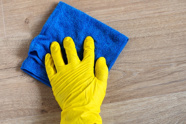 Hand wearing an yellow rubber glove washing a laminate flooring with a blue wet cloth