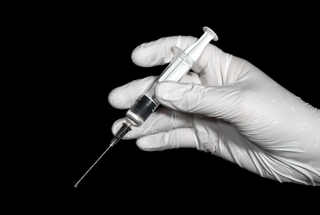 A hand in a white latex glove holds a syringe