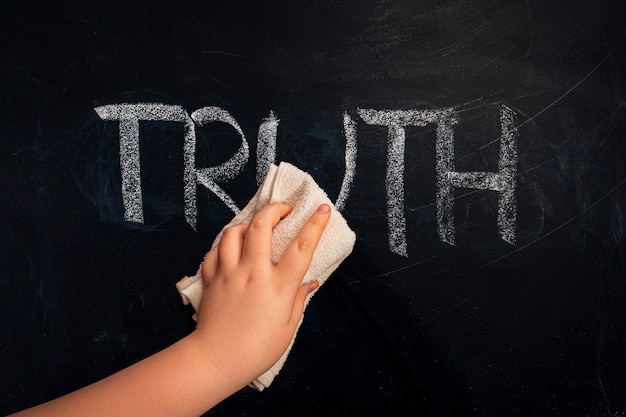 Hand wiping off chalk word truth on chalkboard using rag