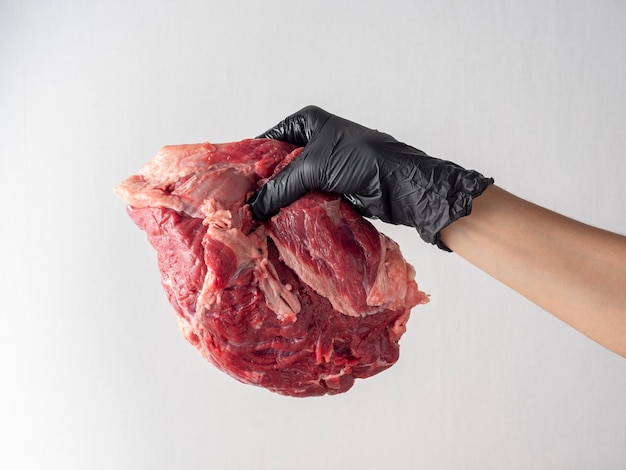 A hand with a black glove holds a piece of fresh raw marbled beef on a light background