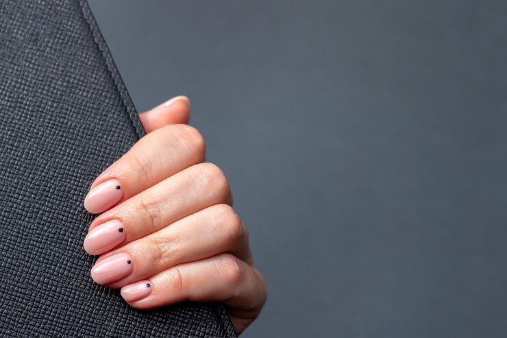 Hand with black leather surface with pink nude nails on gray