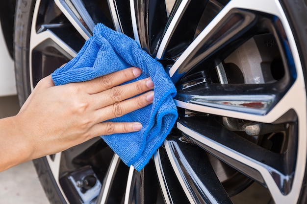 Hand with blue microfiber cloth cleaning car wheel.