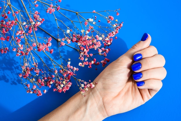 Hand with blue nails on dried flowers background. Female manicure. glamorous beautiful manicure. Winter or autumn manicure in blue. Fashionable Nail Gel Polish Color