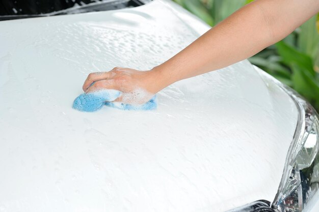 hand with blue sponge washing white car