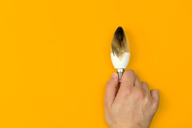 Hand with burned LED light bulb. Concept of electrical short circuit. Burning wire in house, dangerous, failure. Home safety. Top view, orange background photo