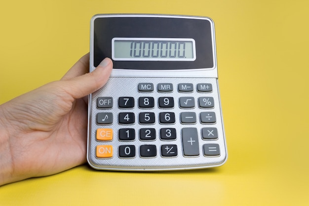 Hand with a calculator on a yellow background. The concept of finance, business, money, accounting, savings