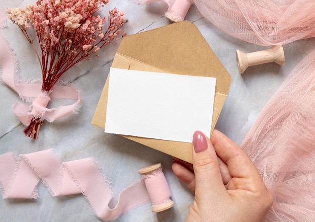 Hand with card and envelope with pink flowers and ribbons