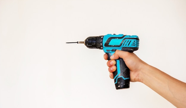 Hand with cordless screwdriver and drill isolated on white background. Twists screws into the board.