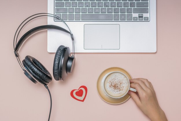 Hand with a Cup of coffee, a laptop and headphones on a coral . Job. Freelance.