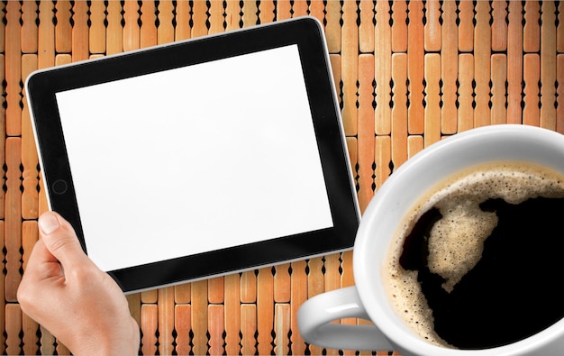 デジタル タブレットと一杯のコーヒーを持つ手