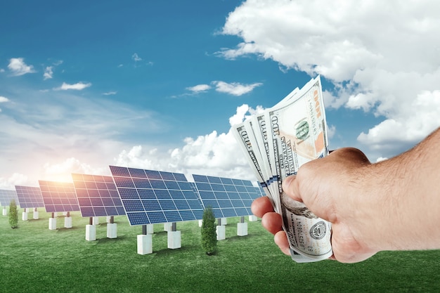 Photo hand with dollars on the background of solar panels.. solar energy business, the cost of green