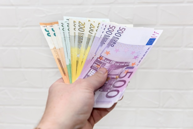 Hand with euro banknotes upon white brick wall close up