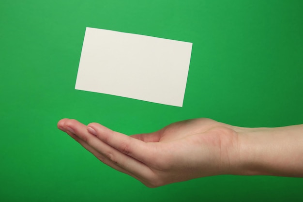 Hand with flying business card on green background