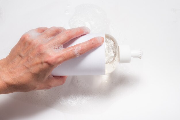 Hand with foam holding bottle with dish washing liquid