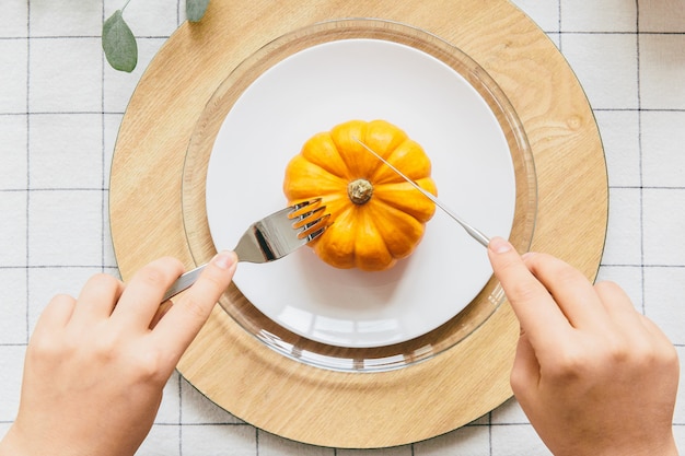 Hand with fork and knife cutting yellow pumpkin on white plate