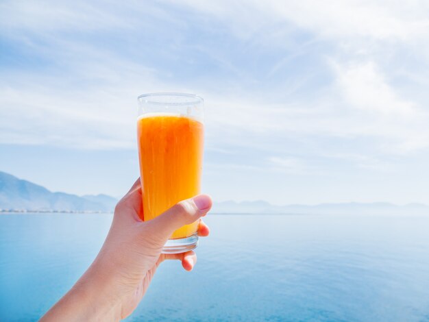 Рука со свежим вкусным свежевыжатым соком спелых апельсинов в стакане.