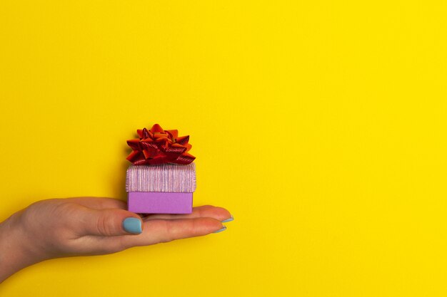 Hand with a gift box on yellow background with free space for text list of presents