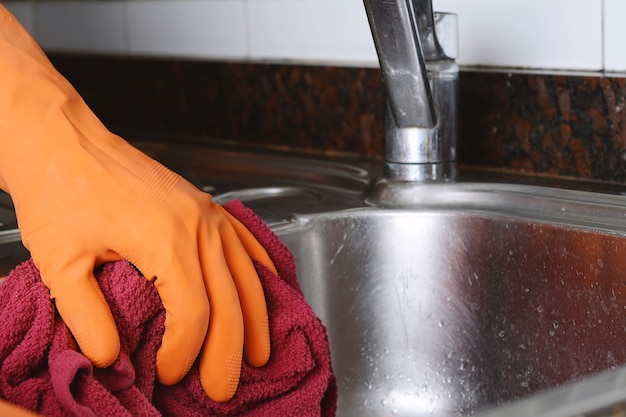 Hand with gloves wiping stainless steel sink with cloth