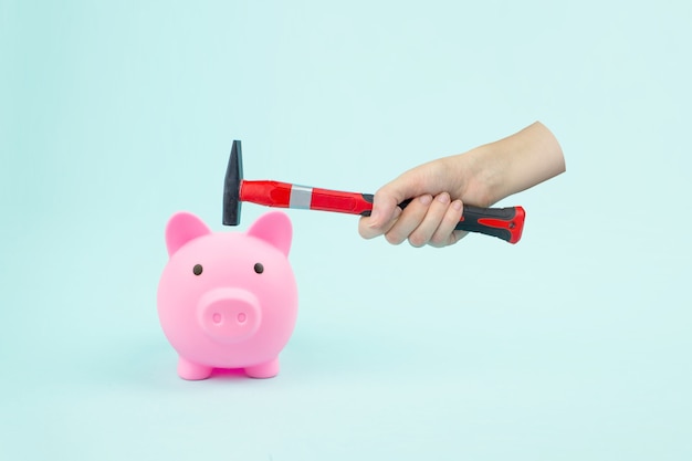 Hand With Hammer And Piggy Bank on blue background. Financial insecurity concept image.