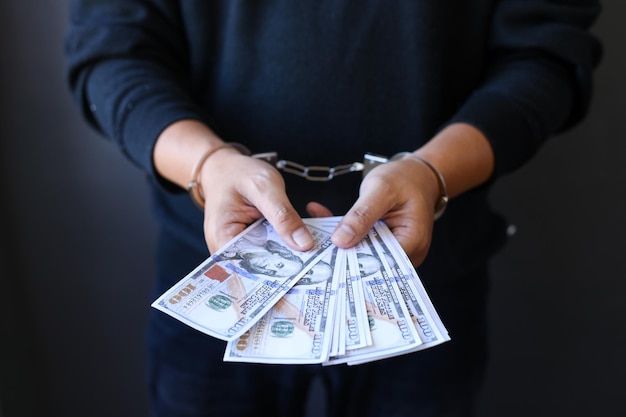 Hand with handcuffs and US dollars against dark background concept of dependence on money Crime in