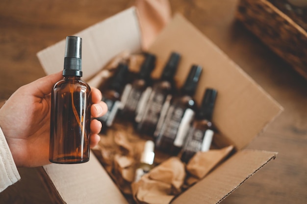 A hand with a jar of oil against the background of a box with funds unpacking the parcel