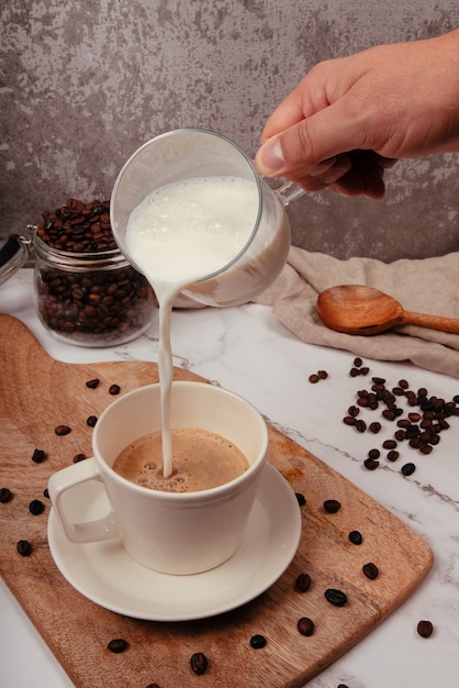 커피 컵 위에 우유를 붓는 주전자와 손