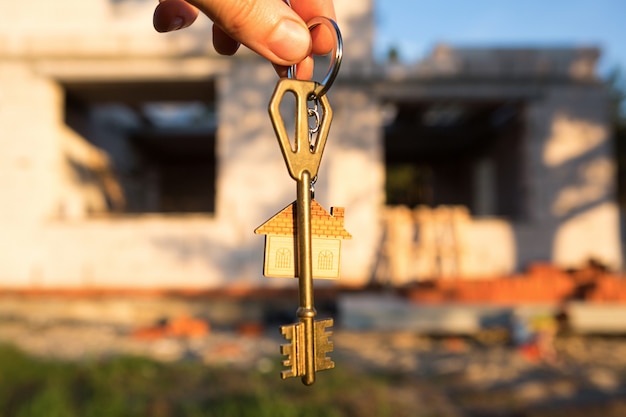 Hand with the key to the future house on the background of a construction site and walls
