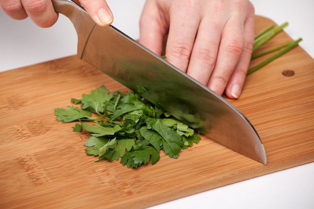 Hand with a kitchen knife cuts and chops parsley on a wooden cutting board