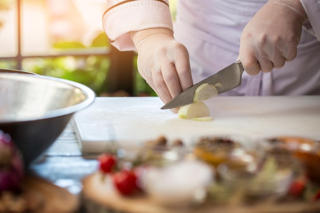 Hand with knife cuts onion. White vegetable on cooking board. Ingredient of spicy soup. Preparation of meal in restaurant.