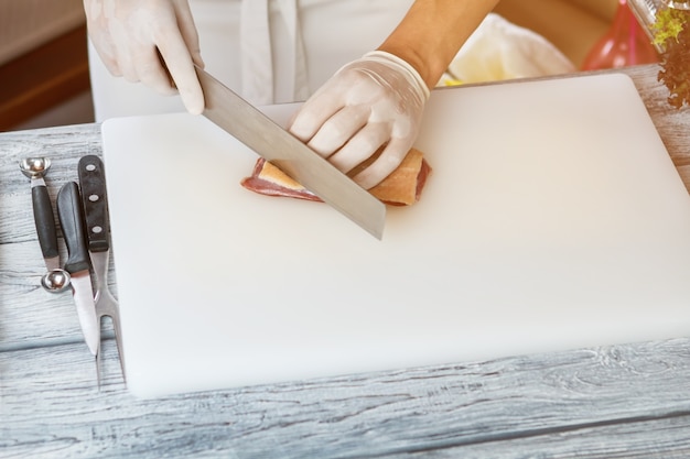 Hand with knife cutting meat meat on white cooking board key ingredient for steak duck meat with skin