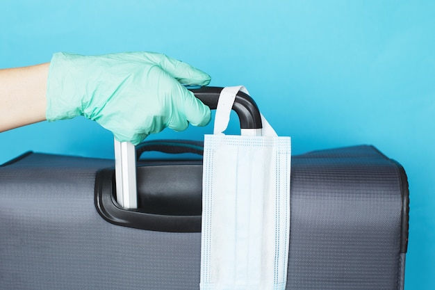 Hand with a luggage bag and medical mask isolated on a blue background