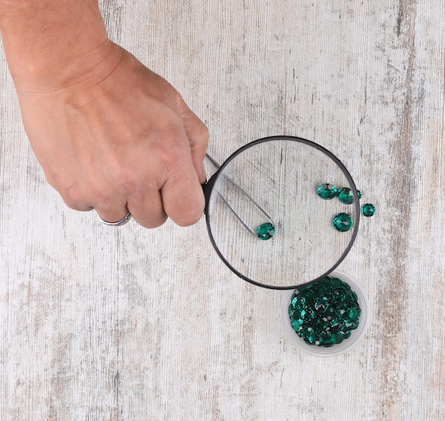 hand with a magnifying glass looks at the emerald