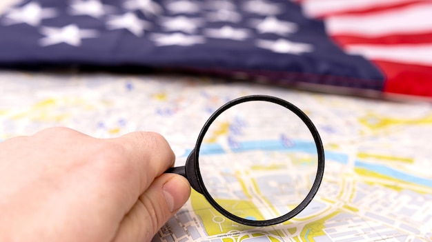 A hand with a magnifying glass on a map with the flag of the United States in the background concept of travel in the national territory